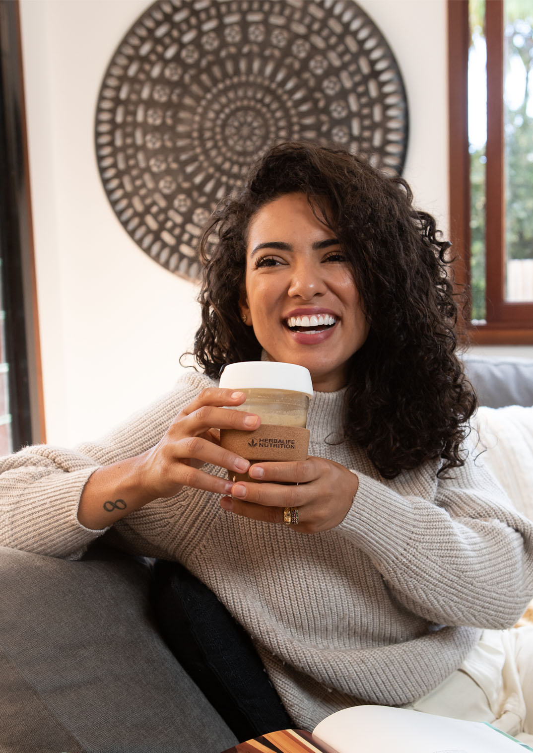 Image of woman smiling and drinking from a Herbalife Nutrition cup in front of an open book