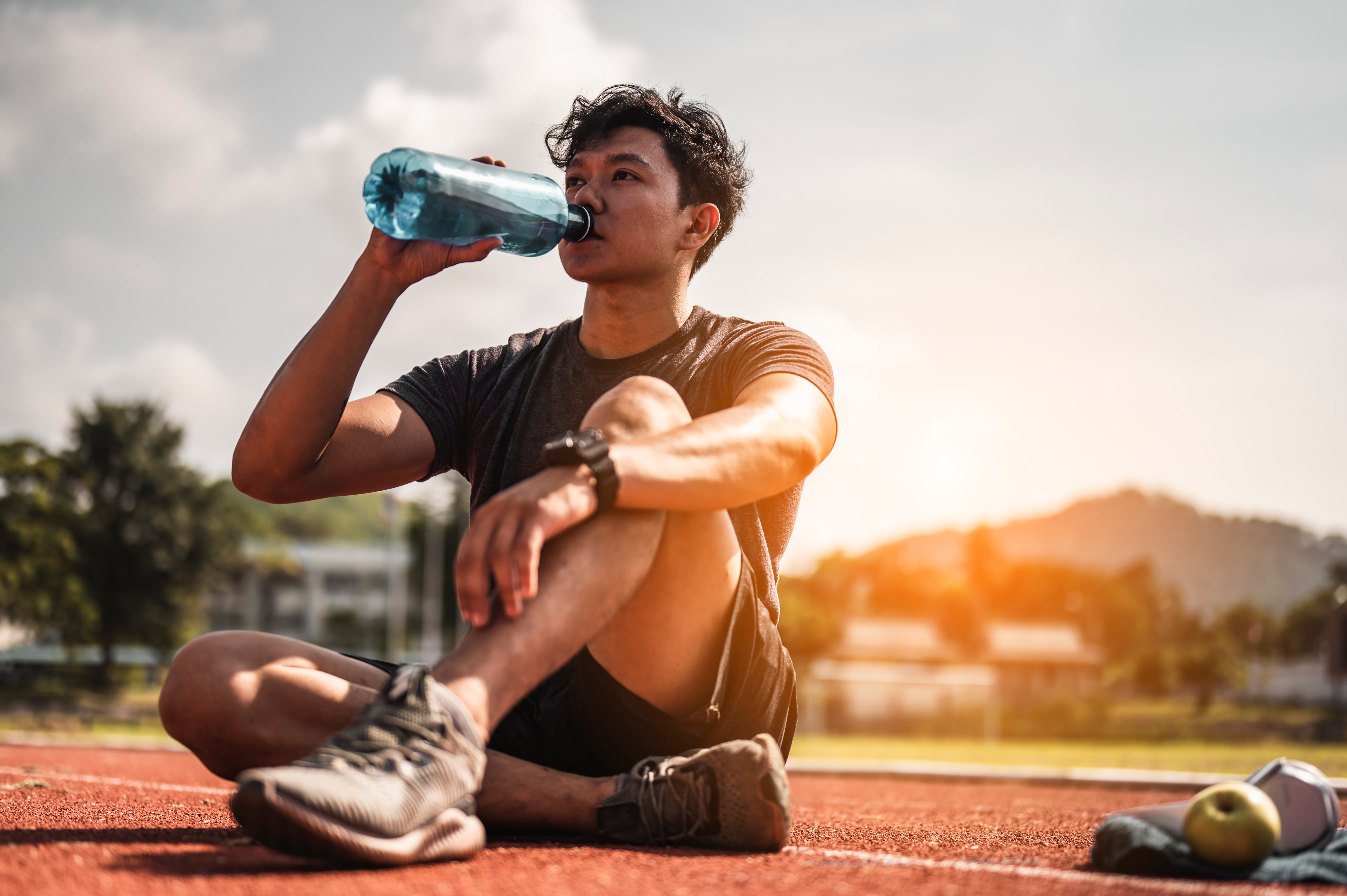 The young man wore all parts of his body and drink water to prepare for jogging on the running track around the football field.