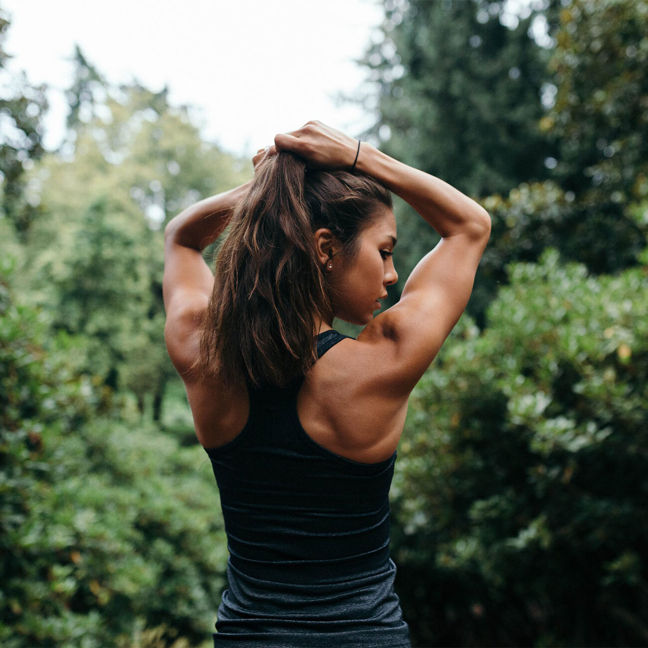 Frau hält sich während des Workouts draußen die Haare zusammen und schaut schaut dabei über ihre Schulter