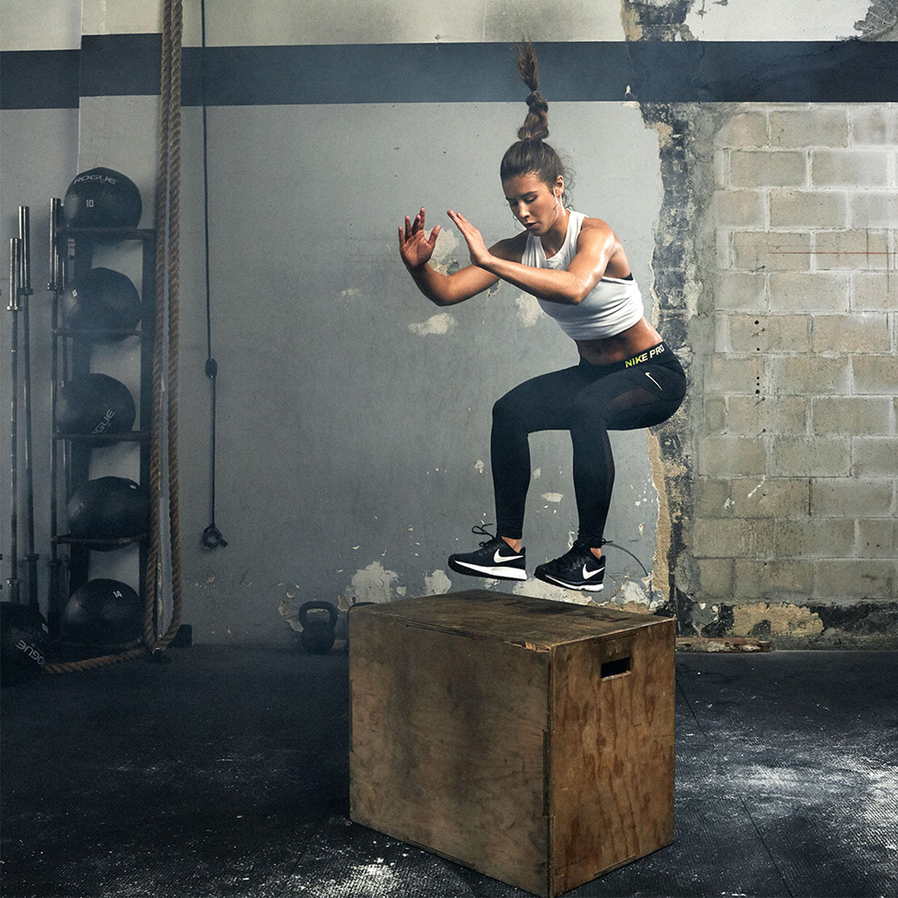 sportlerin hüpft auf eine cross-fit box aus holz während dem workout im fitnessstudio