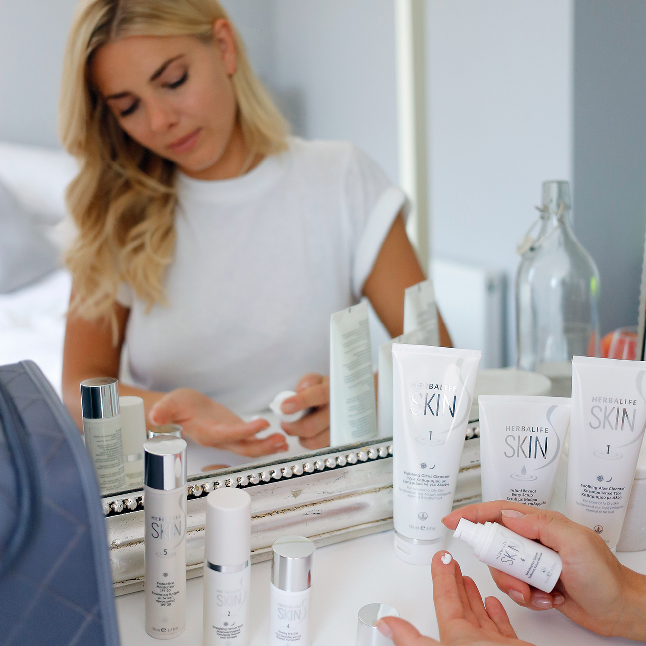 Μια γυναίκα μπροστά σε καθρέπτη χρησιμοποιεί τα προϊόντα της σειράς Herbalife Skin