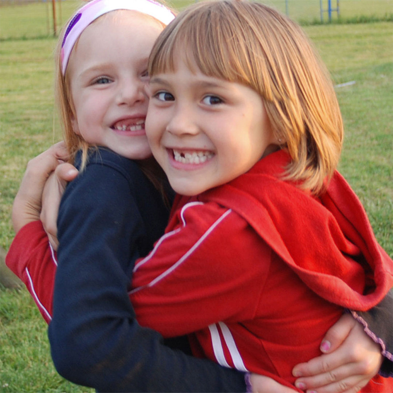 δύο παιδιά αγκαλιάζονται και χαμογελούν στη παιδική χαρά σε ένα σπίτι της Herbalife Nutrition.