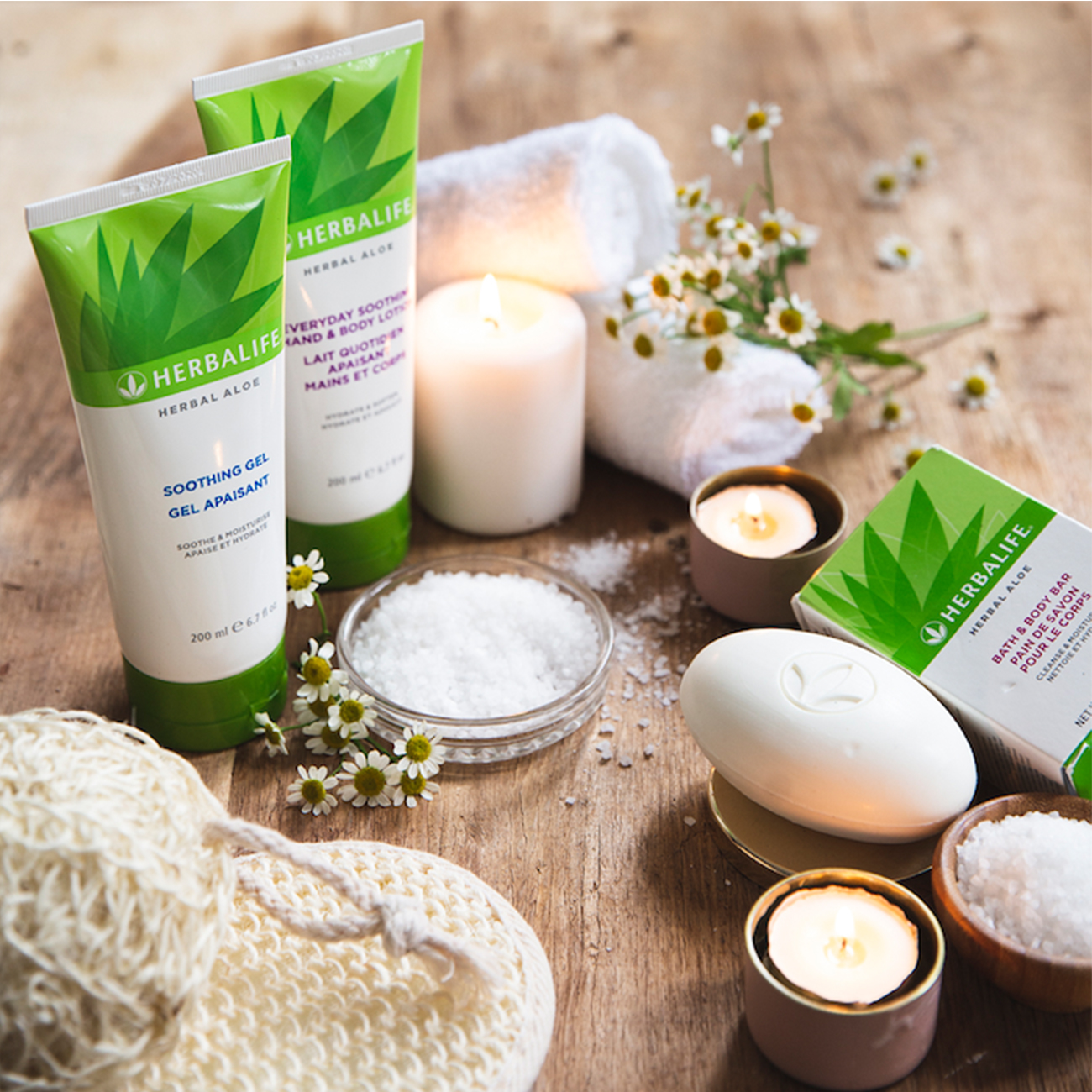 herbal aloe skin and hair products displayed on a wooden table with towels and candles