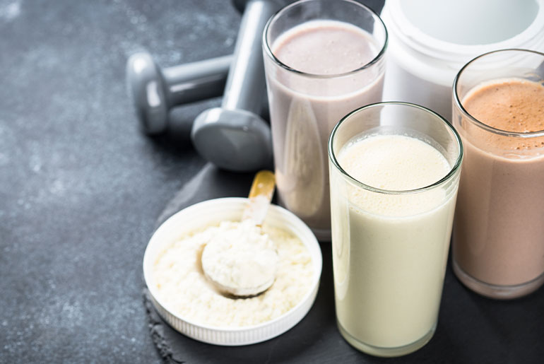 Angle shot of dairy protein powder, protein shakes and dumbbells on black concrete surface