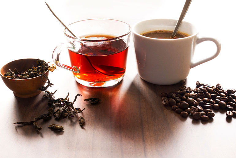 Angle shot of a cup of tea and a cup of coffee along with tea leaves and coffee beans