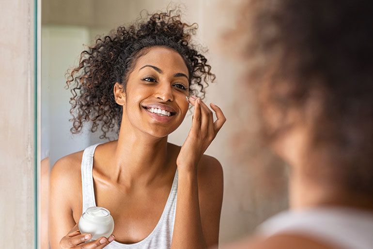An indoors shot of a woman applying moisturiser in front of a mirror
