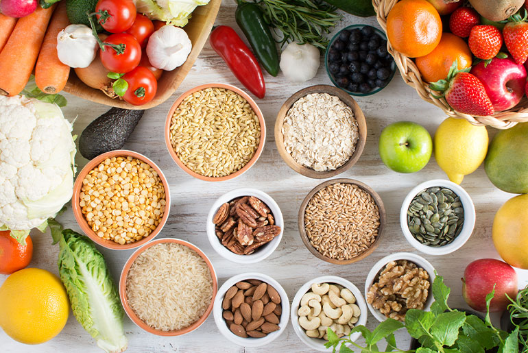 Overhead shot of fibre-rich nuts, legumes, fruits and vegetables on a white wood surface
