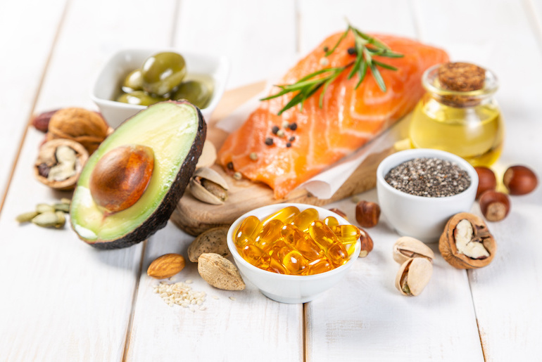 Angle shot of Omega-3 capsules and Omega-3-rich foods on a white wood surface