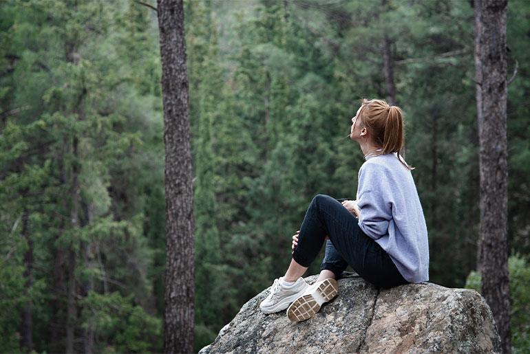 An outdoors shot of a woman in sports clothes gazing at the trees in a forest