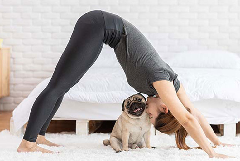Woman doing a yoga workout at home and kissing her dog