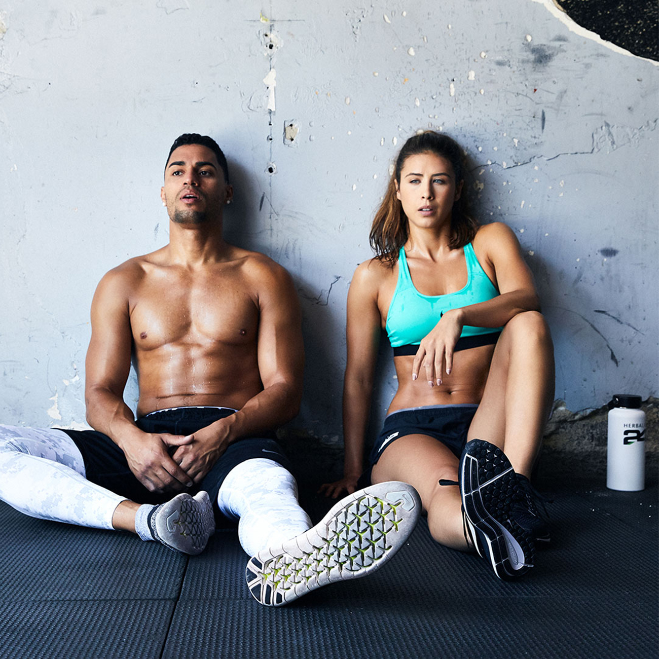 Moški in ženska v telovadnici sedita na tleh in počivata po intenzivni vadbi.